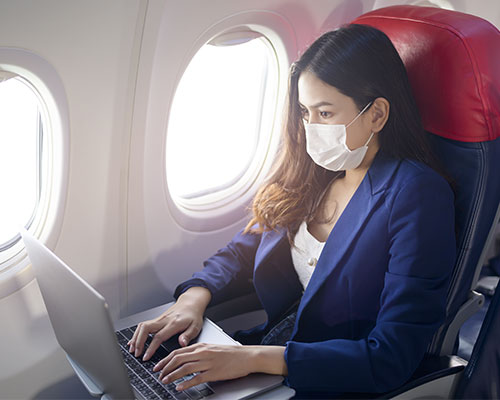 woman wearing a mask using a laptop on an airplane